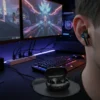 Airox E5 wireless earbud worn by a gamer at a vibrant gaming desk, with open charging case.