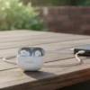 White Audionic Airbuds 495, one in ear, charging case with earbuds connected to power bank on an outdoor wooden table.