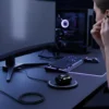 User inserting Mars MB-10 wireless earbud at gaming desk with wireless charging case, PC, and monitor.